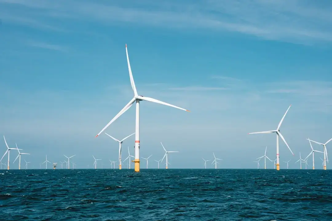 An aerial drone view of a large-scale offshore wind farm with turbines standing in the deep blue ocean water.