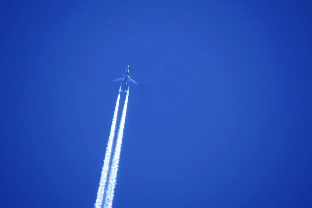Long white aircraft contrails streaking across a clear bright blue sky
