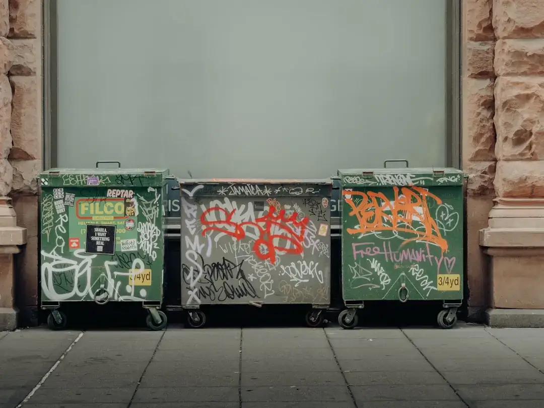A row of various colorful charity donation bins and collection containers for clothing and shoes located outdoors.