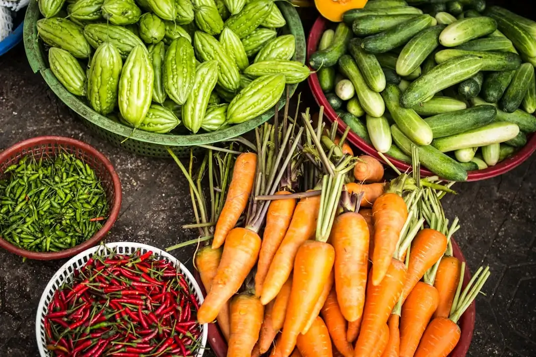 A colorful variety of fresh organic vegetables including greens, carrots, and peppers arranged on a wooden surface.