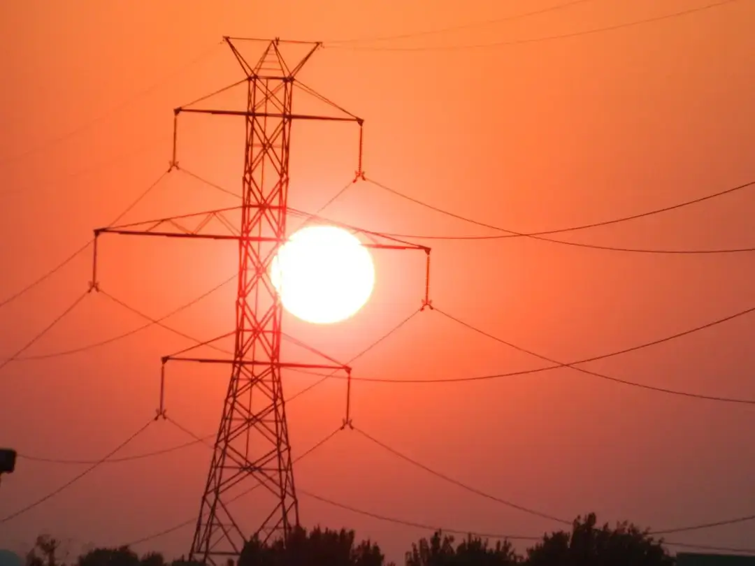A row of high voltage power line towers stretching across a horizon under a clear sky.