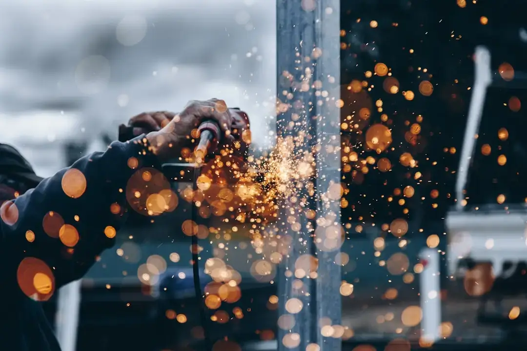 Close-up of a professional welder working on metal with bright orange sparks flying in an industrial setting