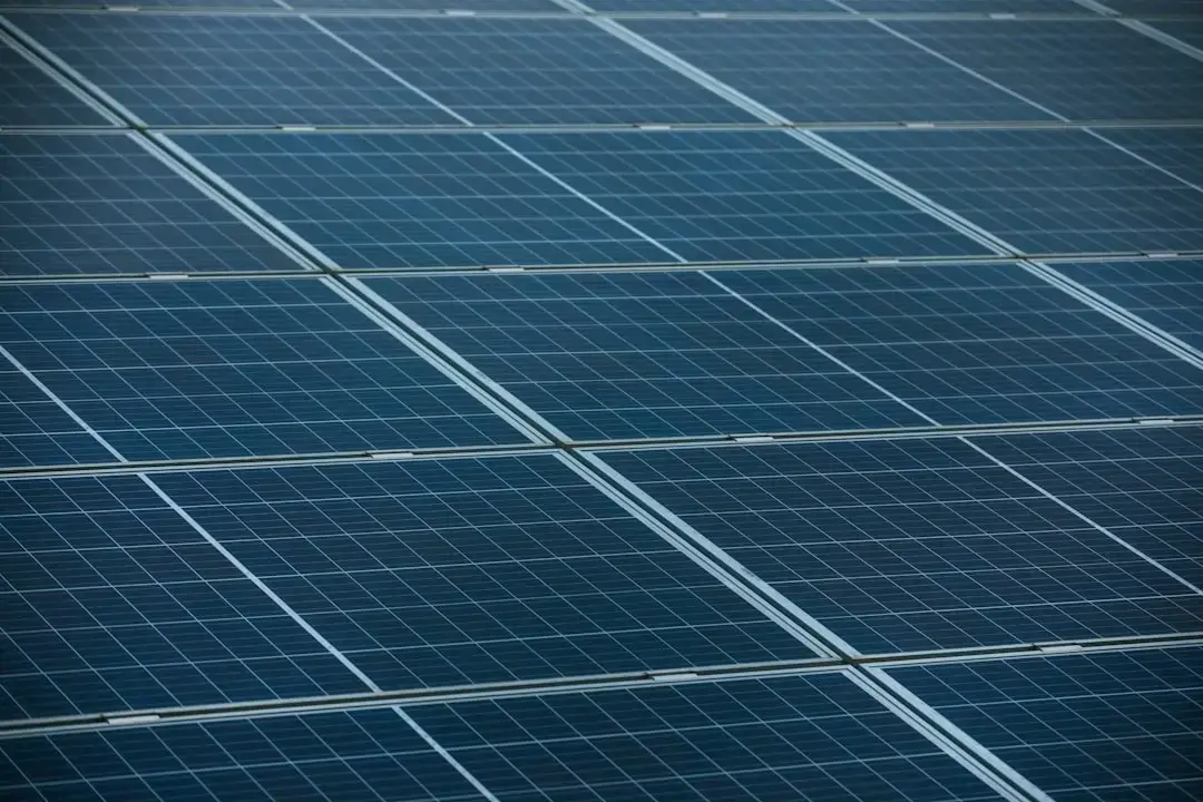 A vast array of modern blue solar panels installed in a rural field under a clear sky representing renewable energy.