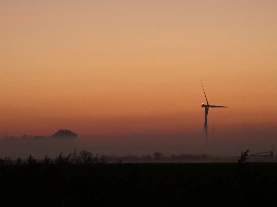 A sleek modern wind turbine standing tall in a green field against a clear sky, representing sustainable energy.
