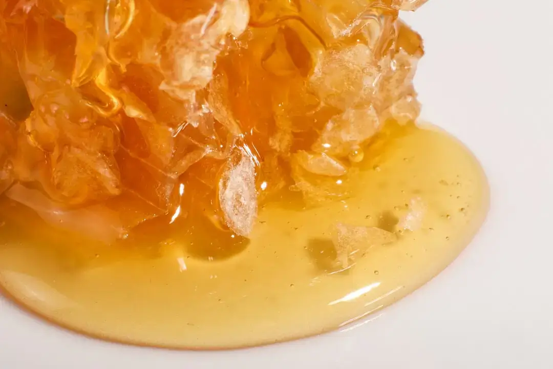Ein klares Glasgefäß gefüllt mit goldenem Bio-Honig mit einem Honiglöffel aus Holz auf einem rustikalen Hintergrund.