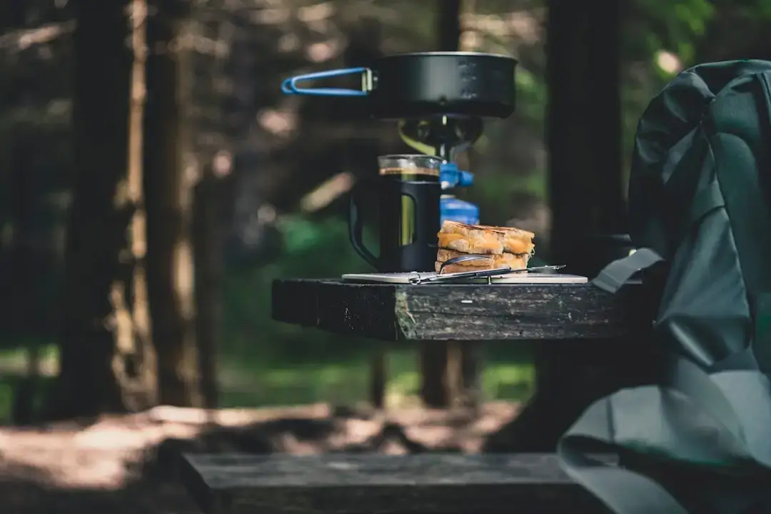 A portable camping gas canister attached to a compact camp stove burner on a rustic surface outdoors.