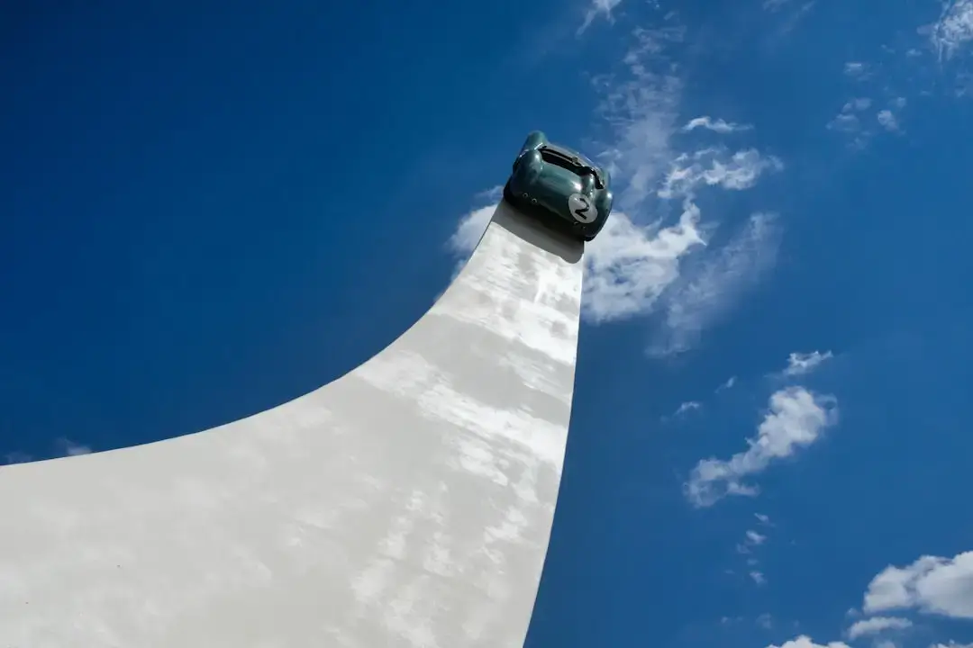 An electric vehicle driving past a row of tall white wind turbines on a green hill under a clear sky.