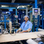 Factory worker smiles while operating machinery.