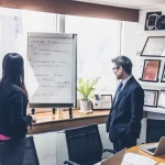 man in black jacket standing beside white board