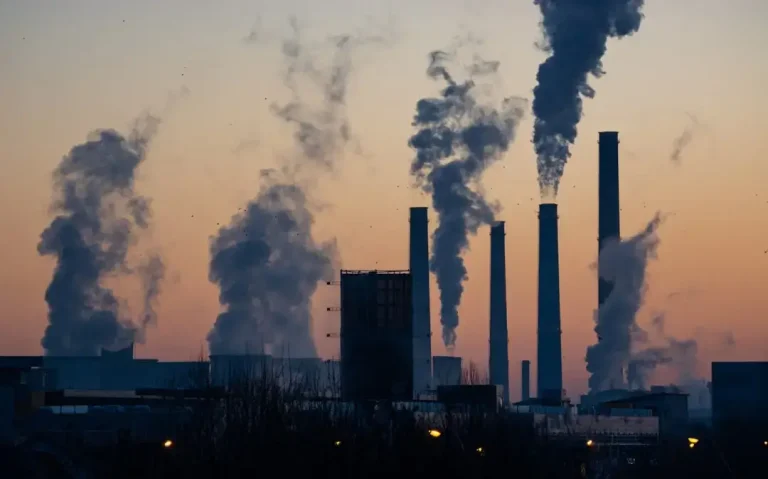 Large industrial factory chimneys emitting thick smoke into the atmosphere, representing global greenhouse gas emissions.