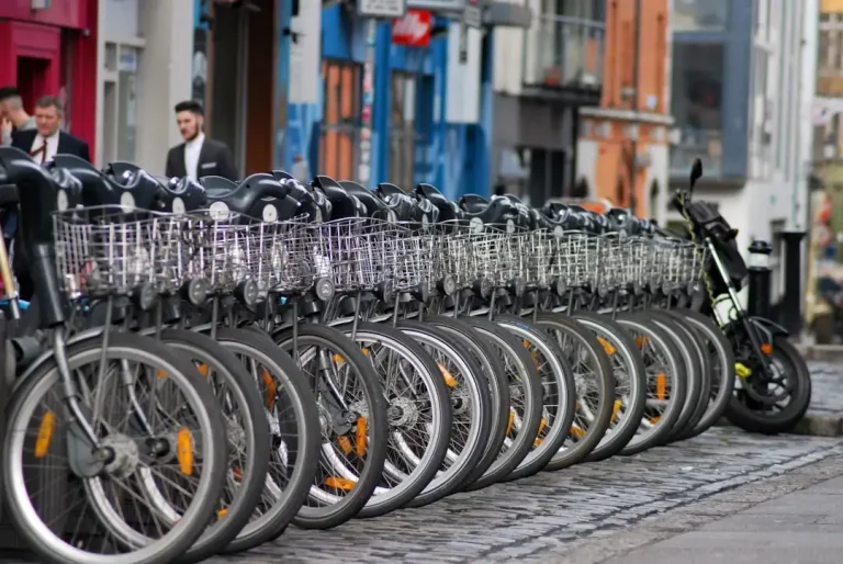 A row of modern city bicycles parked at a public rental station in an urban environment.