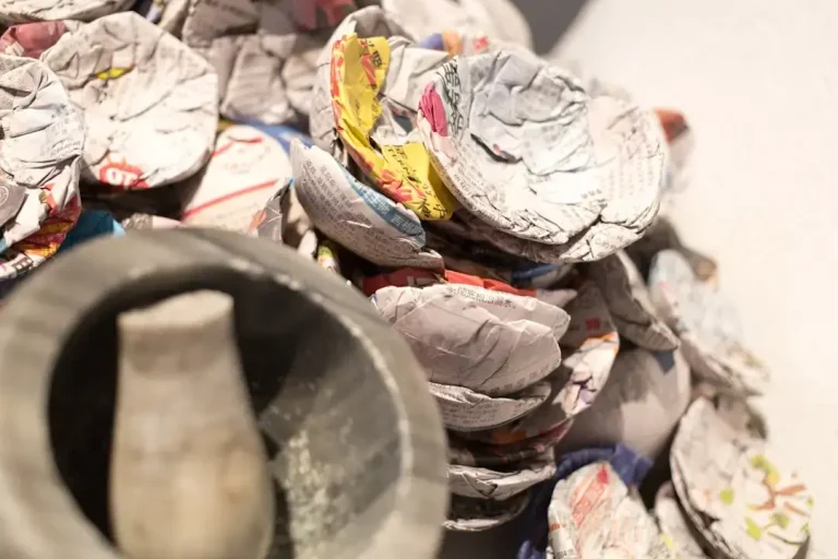 Close-up of grocery store receipts held in hand over colorful recycling bins, illustrating proper waste segregation.