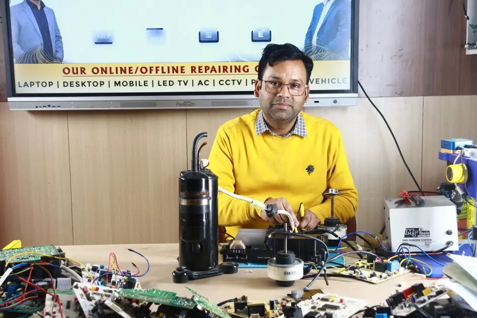 Mężczyzna zajmuje się naprawą klimatyzatora w ośrodku szkoleniowym w Nowym Delhi, otoczony elementami elektronicznymi.