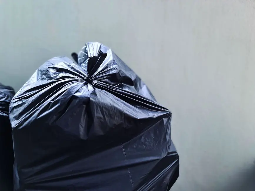 Zbliżenie zdjęcie czarnej torby na śmieci wykonanej z plastiku na tle gładkiej ściany betonowej, podkreślające zarządzanie odpadami.