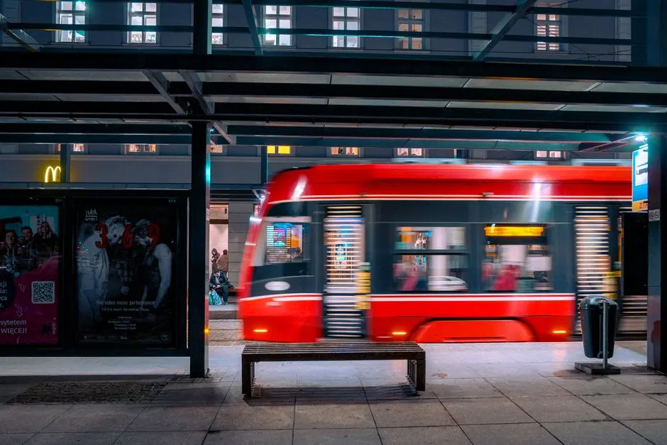 Dynamiczne nocne ujęcie czerwonego tramwaju w ruchu na nowoczesnym przystanku tramwajowym, ukazujące życie miejskie w Katowicach.