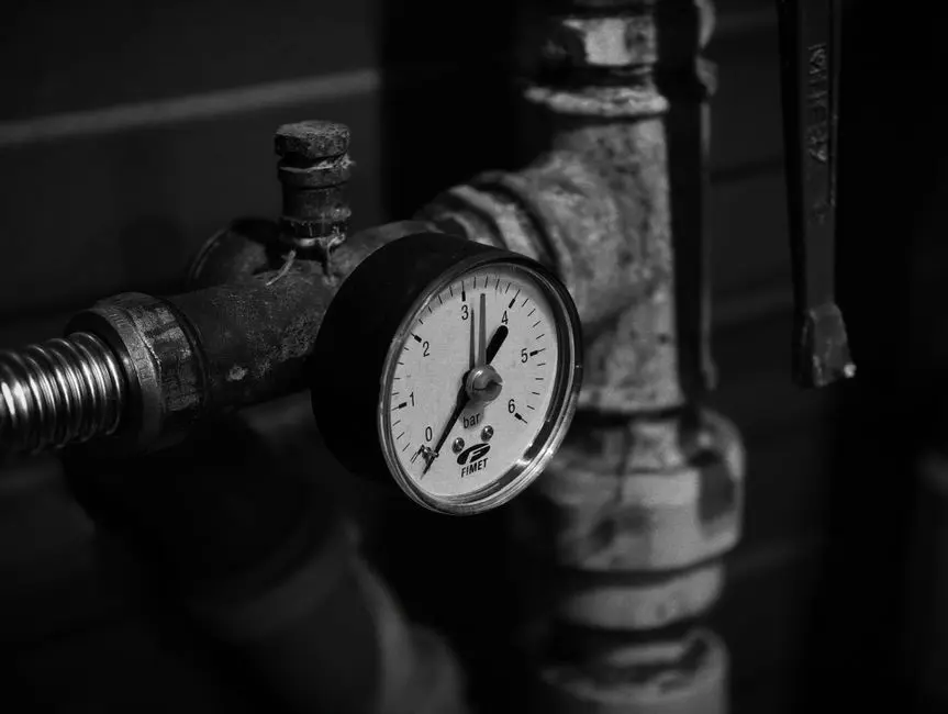 Zbliżenie zabytkowego manometru na rurach przemysłowych w trybie monochromatycznym.